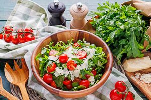 Rucola-Salat mit Kirschtomaten und gehobeltem Parmesan in einer Holzschale frisch servieren