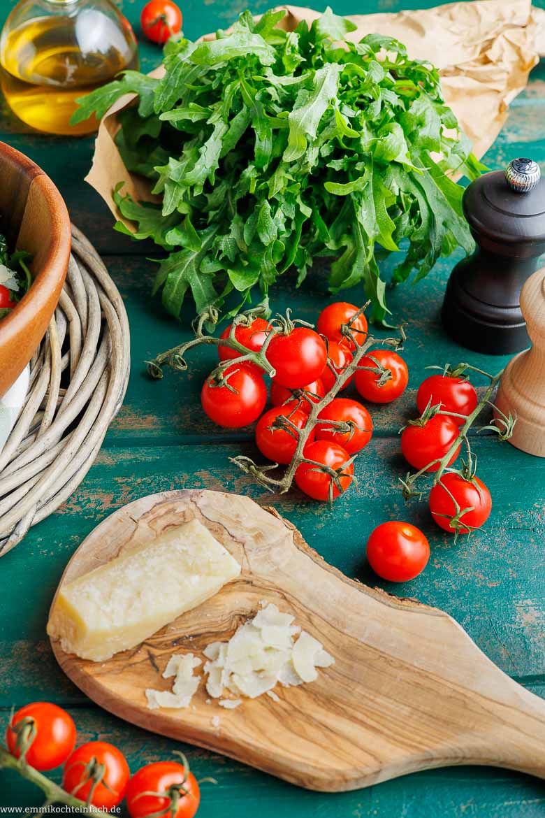 Frische Zutaten für Rucola-Salat: Rucola, Kirschtomaten und gehobelter Parmesan