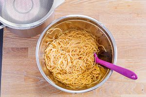 Nasse Spaghetti in einer Sch&uuml;ssel mit dem Dressing vermischt