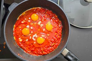 Eier in die Mulden im Shakshuka geben