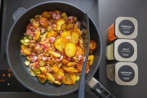 Bratkartoffeln, Zwiebeln, Speck, Cornichons und Gew&uuml;rze vermengen