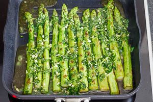 &Ouml;liven&ouml;l mit Kr&auml;utern in die Pfanne &uuml;ber den gr&uuml;nen Spargel gie&szlig;en