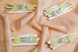 Zucker, Salz, Kr&auml;uterbutter und Limetten auf dem Spargel verteilen und auf das Backpapier legen.
