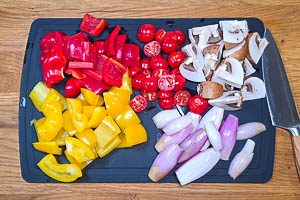Rote und gelbe Paprika in gr&ouml;&szlig;ere W&uuml;rfel schneiden, die Kirschtomaten in H&auml;lften und die Champignons in Viertel schneiden. Schalotten sch&auml;len und halbieren.