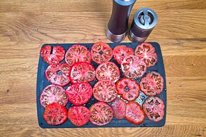 Strauchtomaten horizontal in etwa 1 cm dicke Scheiben schneiden. Anschließend mit Salz und Pfeffer würzen.