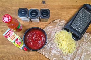 Zutaten für die Tomatensoße verrühren und Käse reiben