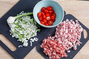 Kirschtomaten, Fr&uuml;hlingszwiebeln, Kochschinken und Salami schneiden