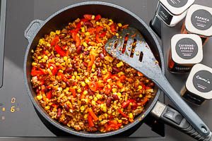W&uuml;rze das Hackfleisch und gib die Zwiebeln, den Knoblauch, die Paprika, den Mais und die Kidneybohnen ebenfalls in die Pfanne.