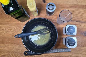 Rühre das Dressing aus Zitronensaft, Zesten, Pflanzenöl, Senf, Salz, Zucker und Pfeffer an.