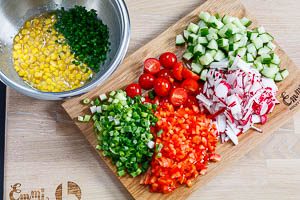 Schneide die Salatgurke, Paprika, Radieschen, Kirschtomaten, Frühlingszwiebeln und Schnittlauch klein. Gib das Gemüse anschließend mit dem Mais zum Dressing.