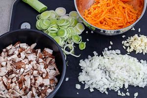 Champignons, Möhren, Lauch, Zwiebeln und Knoblauch schneiden