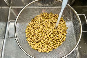 Eingeweichte Linsen in einem Sieb mit kaltem Wasser absp&uuml;len