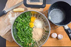 Milch-Masse, Parmesan, Paniermehl, Bärlauch und Eier zu den Brötchenwürfeln geben