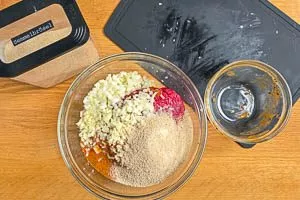 Die Flüssige Würze mit Zwiebeln, Knoblauch und Paniermehl mit dem Hackfleisch vermengen.