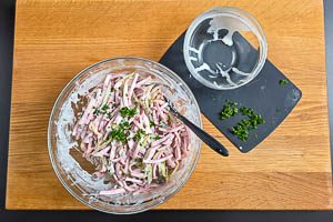Dressing und die Hälfte der Petersilie mit der Fleischwurst und den Gurken vermengen. Vor dem Servieren den Rest der Petersilie darüberstreuen