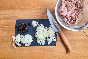 Thunfisch abtropfen lassen und mit einer Gabel zerkleinern, Knoblauch und Zwiebeln würfeln und Oliven in Scheiben schneiden