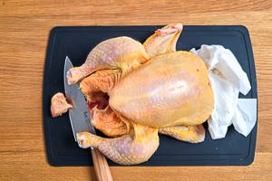 Hähnchen abtupfen, Bürzel abschneiden, Flügel verschränken und Flügelspitze über den Unterarm