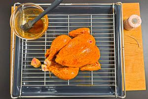 Hähnchen drehen, Beine zusammenbinden und mit Marinade bestreichen und in den Ofen schieben