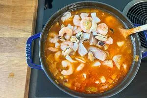 Nach der ersten Garzeit den Fisch und die Meeresfr&uuml;chte dazugeben, Lorbeerbl&auml;tter und Sternanis entfernen, mit Salz, Cayennepfeffer und Orangenschale w&uuml;rzen