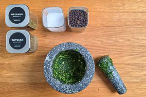 Petersilie, Oregano, Thymian, Meersalz, Pfefferkörner und Knoblauch im Mörser zerstoßen