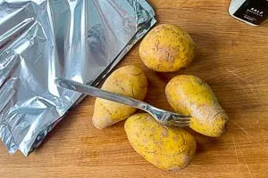 Mit einer Gabel Löcher in die Kartoffeln stechen, dann Alufolie zurechtschneiden