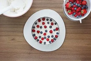 Sahne-Frischk&auml;se-Creme und Beeren auf dem Biskuitboden verteilen