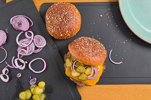Patties mit K&auml;se auf die untere H&auml;lfte legen, mit Gew&uuml;rzgurken und Zwiebeln belegen und dann mit der oberen H&auml;lfte schlie&szlig;en